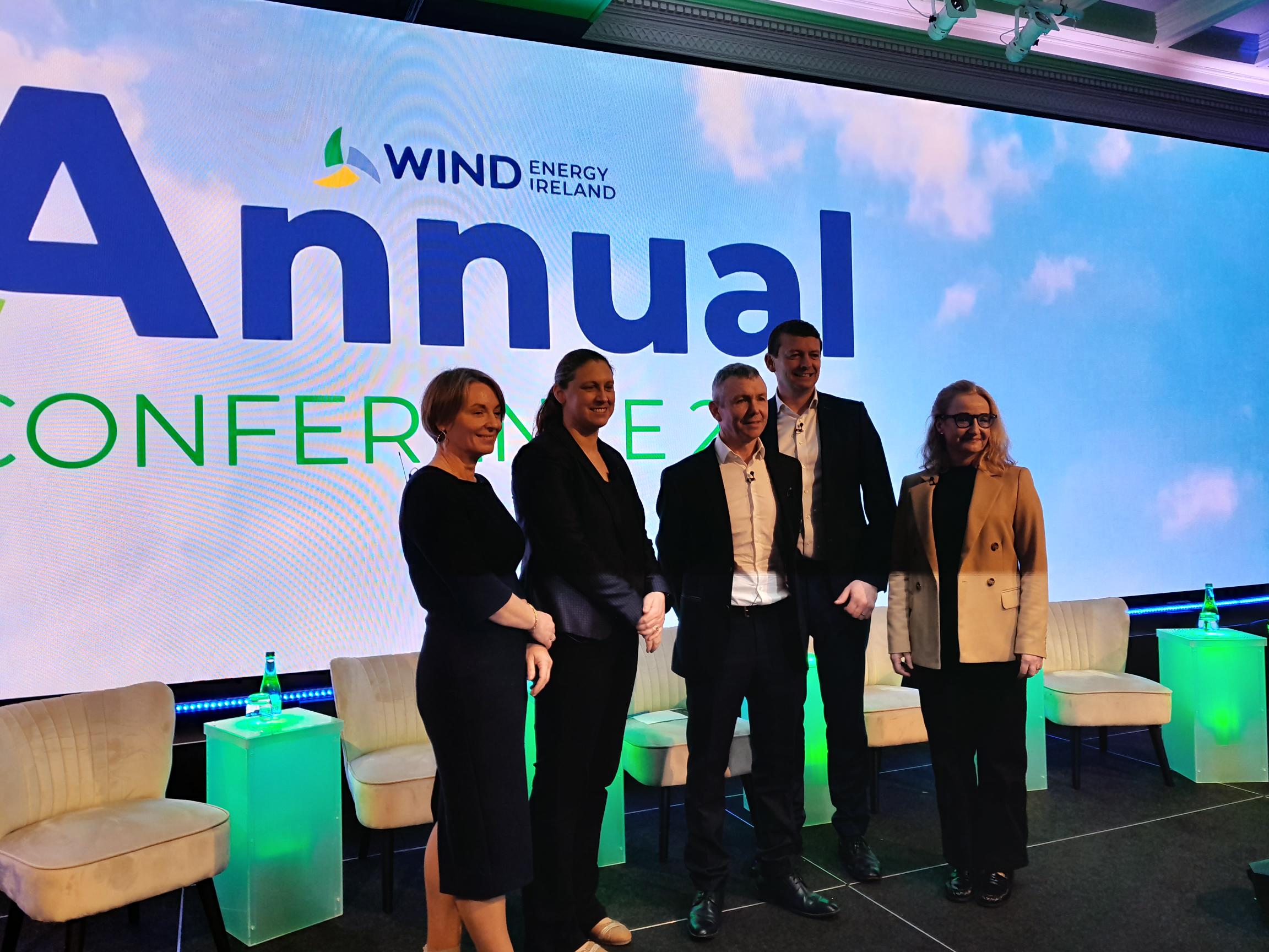 Five people standing in front of a blue background that read: Wind Energy Ireland Annual Conference.